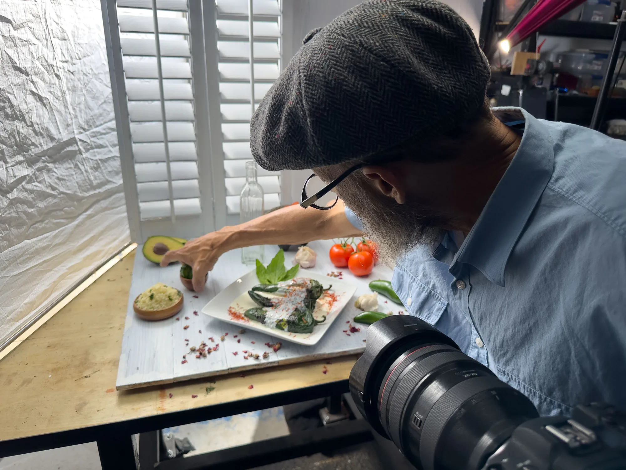 Food stylist arranging avocado and vegetables on a white plate beside a camera lens - Raging Bull Food Photography